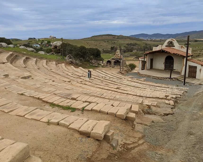 The outdoor amphitheater at Rancho El Refugio with stone-tiered bench seating and a stage before the hills of Baja California