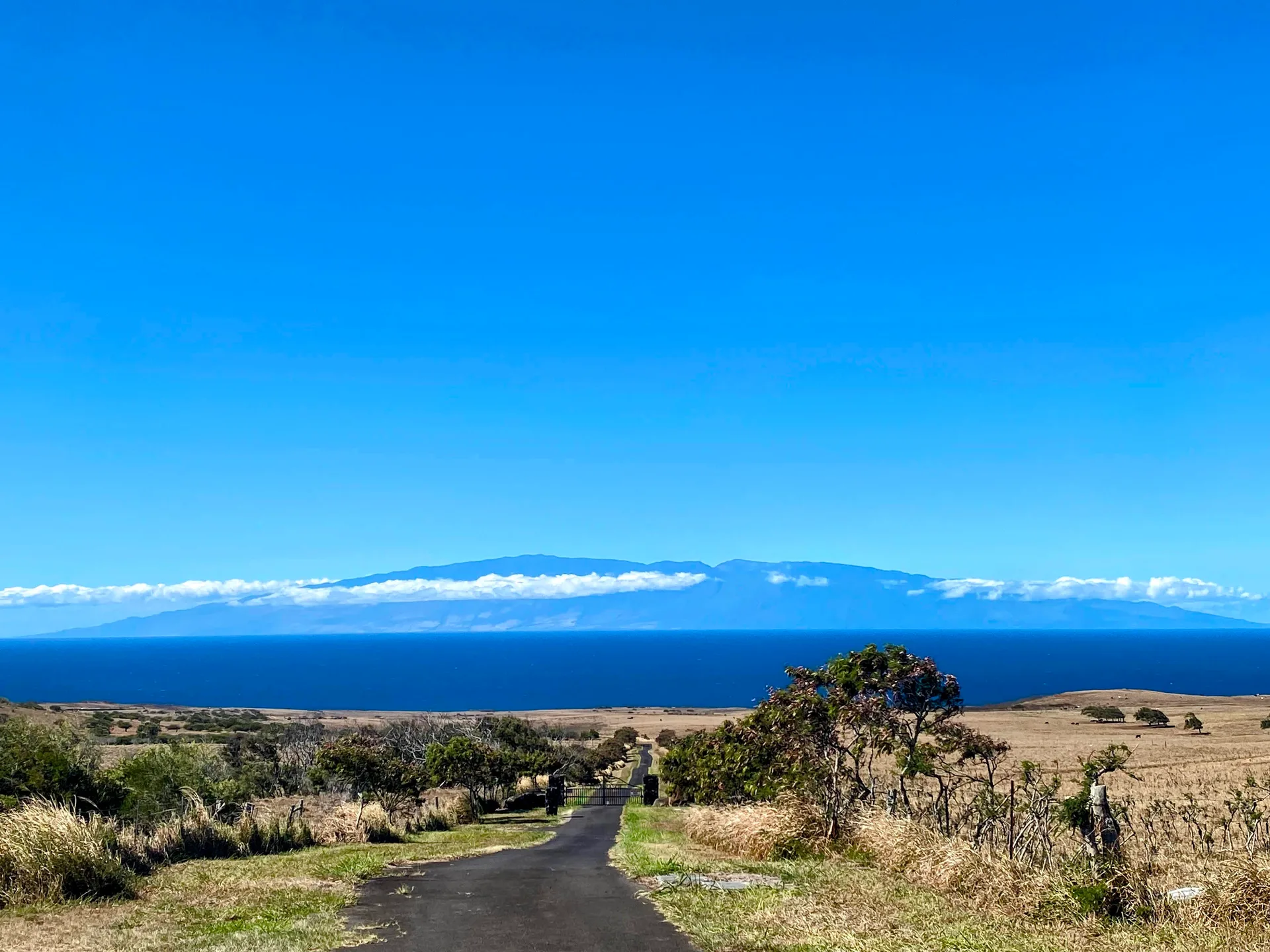 A rural road leading toward the ocean and a distant island mountain range