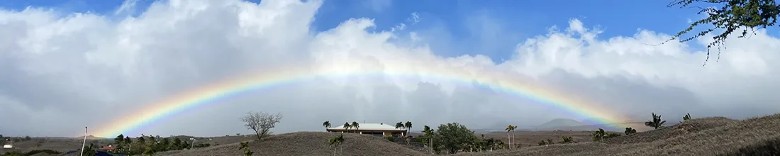 A full rainbow spanning the sky over the dry lava country behind the coast