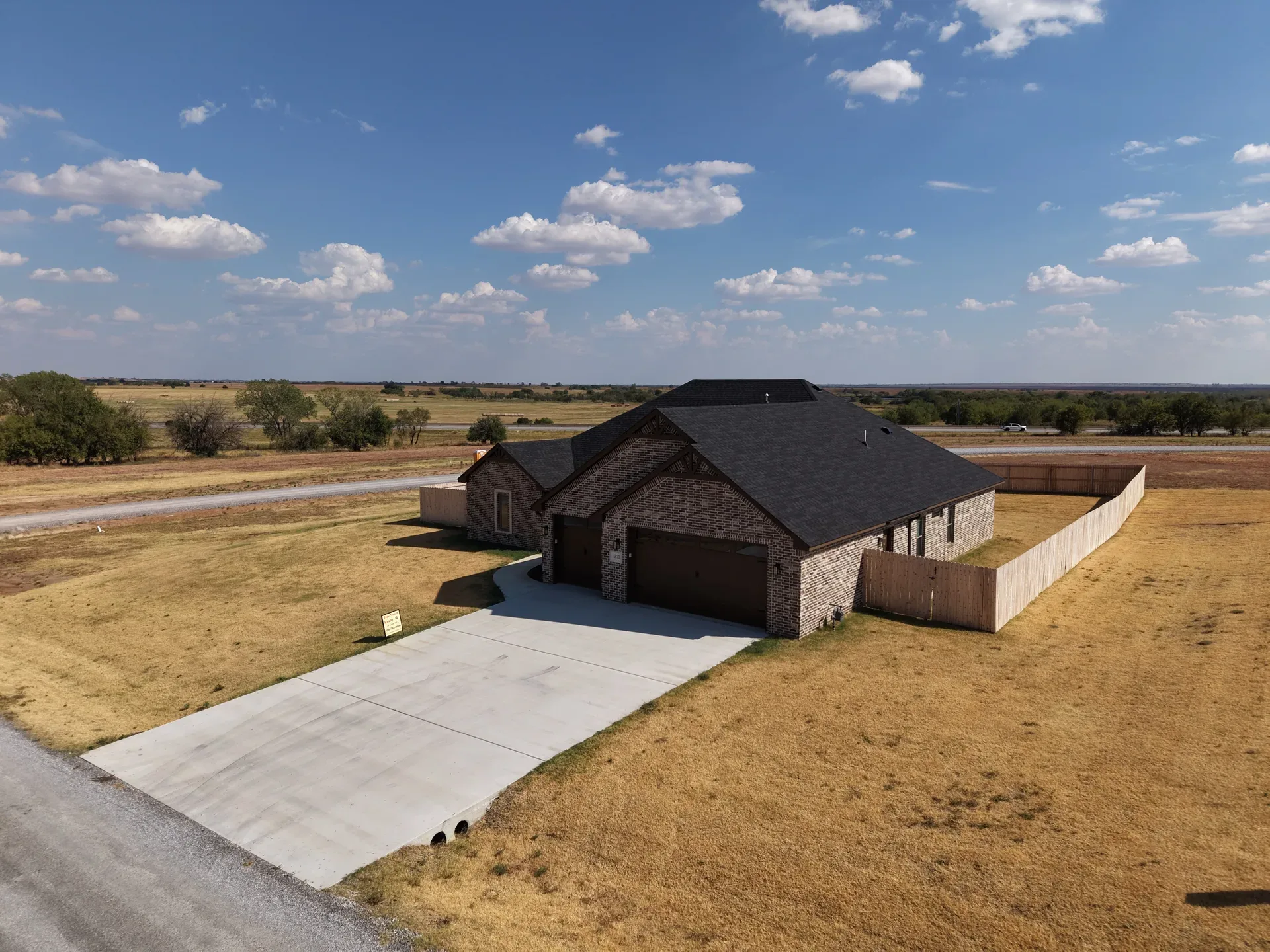 Drone aerial of the brick ranch at 5873 NE Minnow Ln with attached garage, driveway, and open lawn