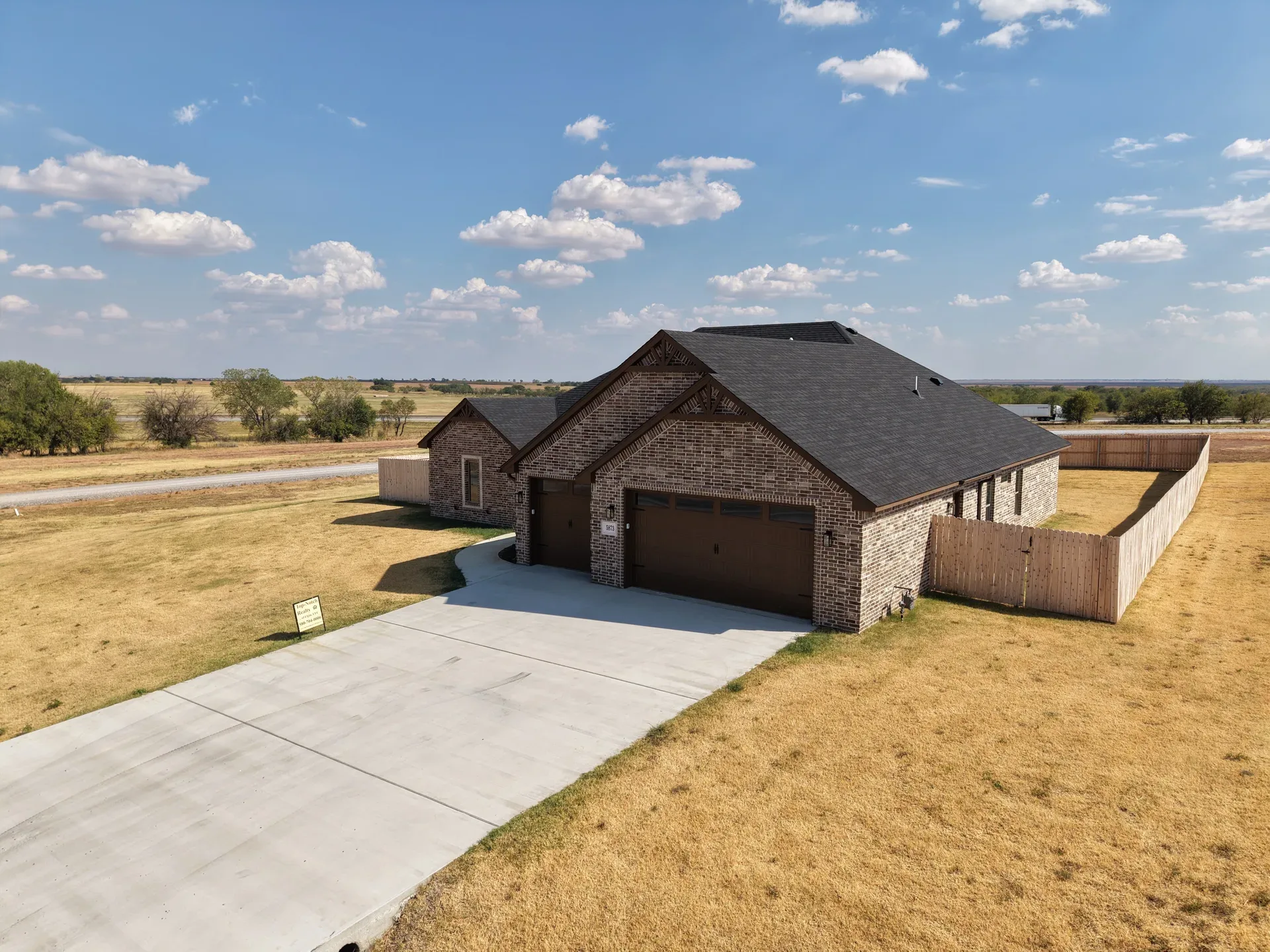 Drone aerial from the front right of the brick ranch, attached garage, and open lawn