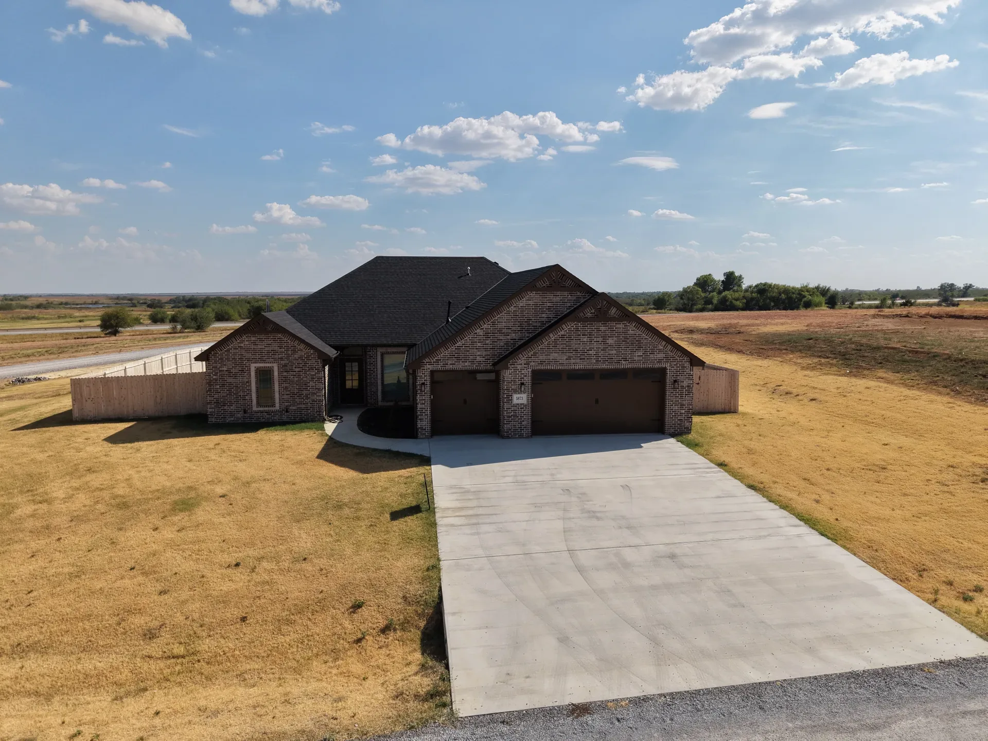 Drone view of the front exterior with driveway, garage doors, and brick facade