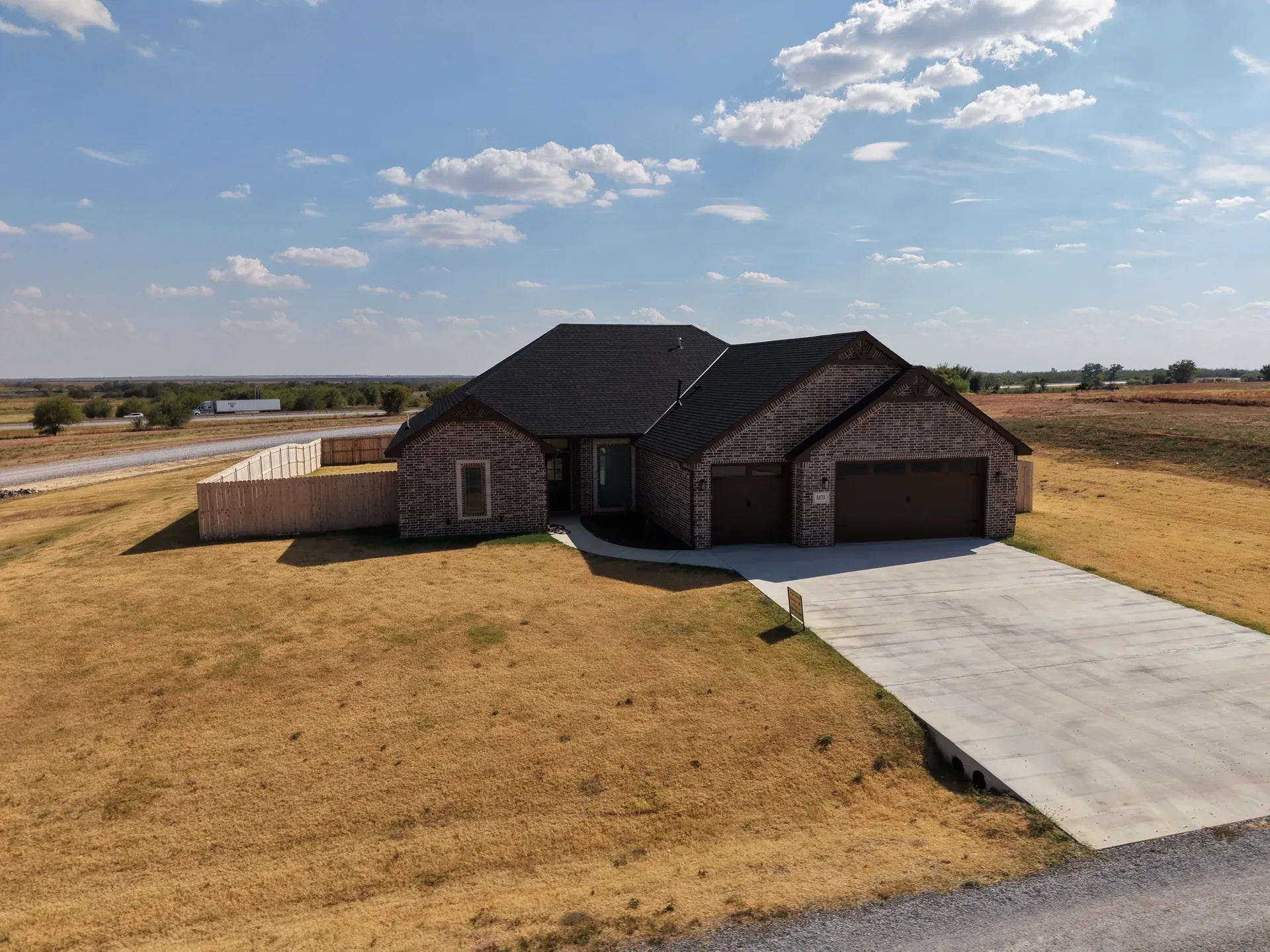 Aerial view of the brick ranch with paved driveway and wooden perimeter fence