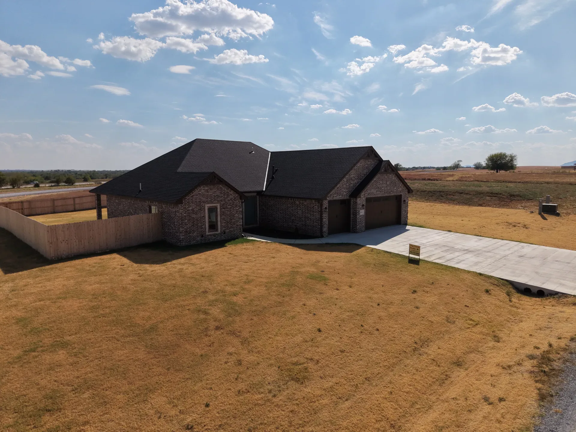 Drone aerial of the home with open lawn, concrete driveway, and wood privacy fence