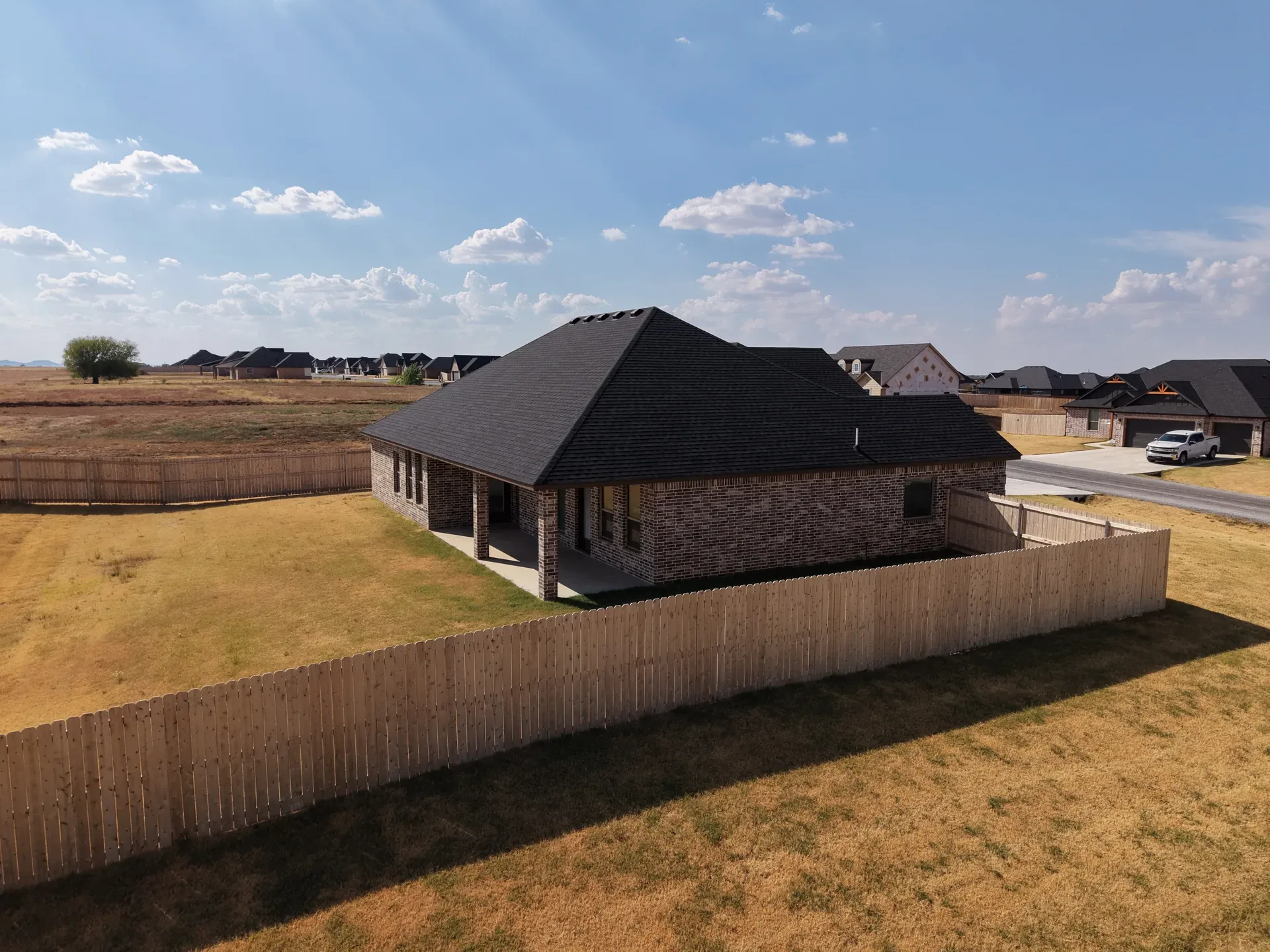 Drone view of the fenced backyard and covered patio behind the brick home