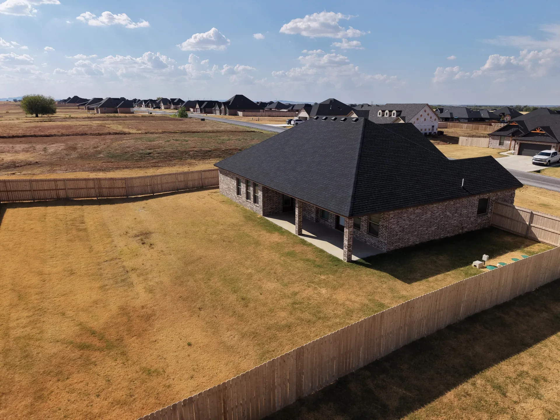 Drone aerial of the large fenced backyard behind the brick home