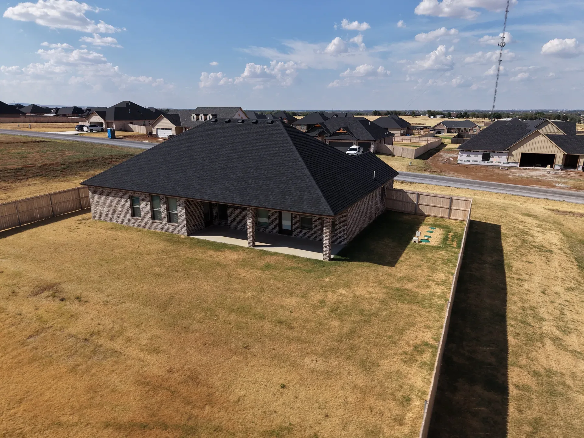 Aerial of the backyard and rear facade with covered patio and fenced yard