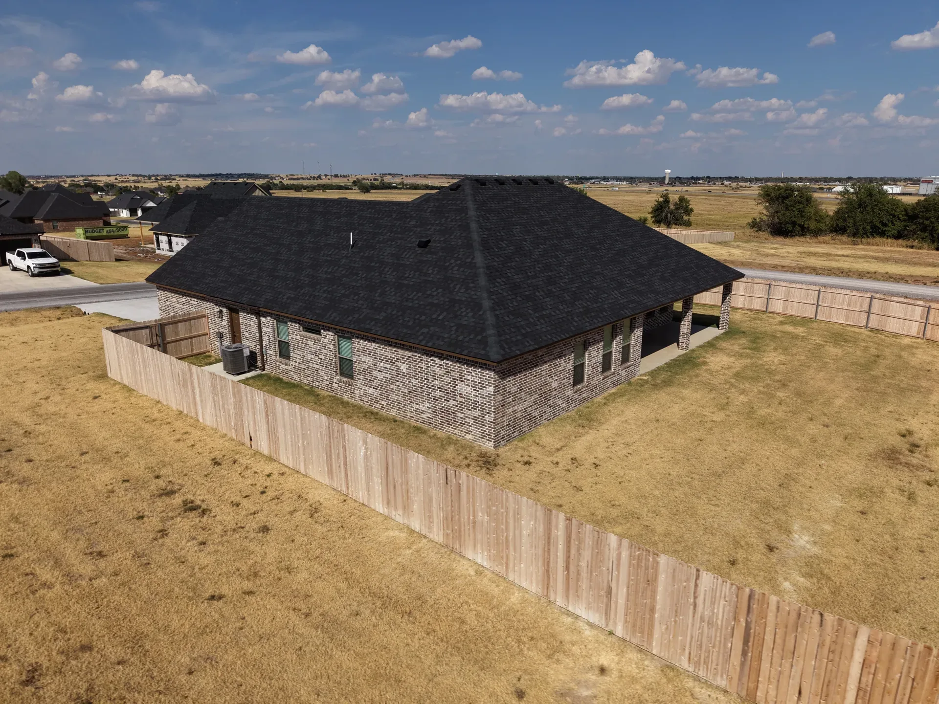 Drone aerial of the rear of the brick home with covered patio and fenced yard