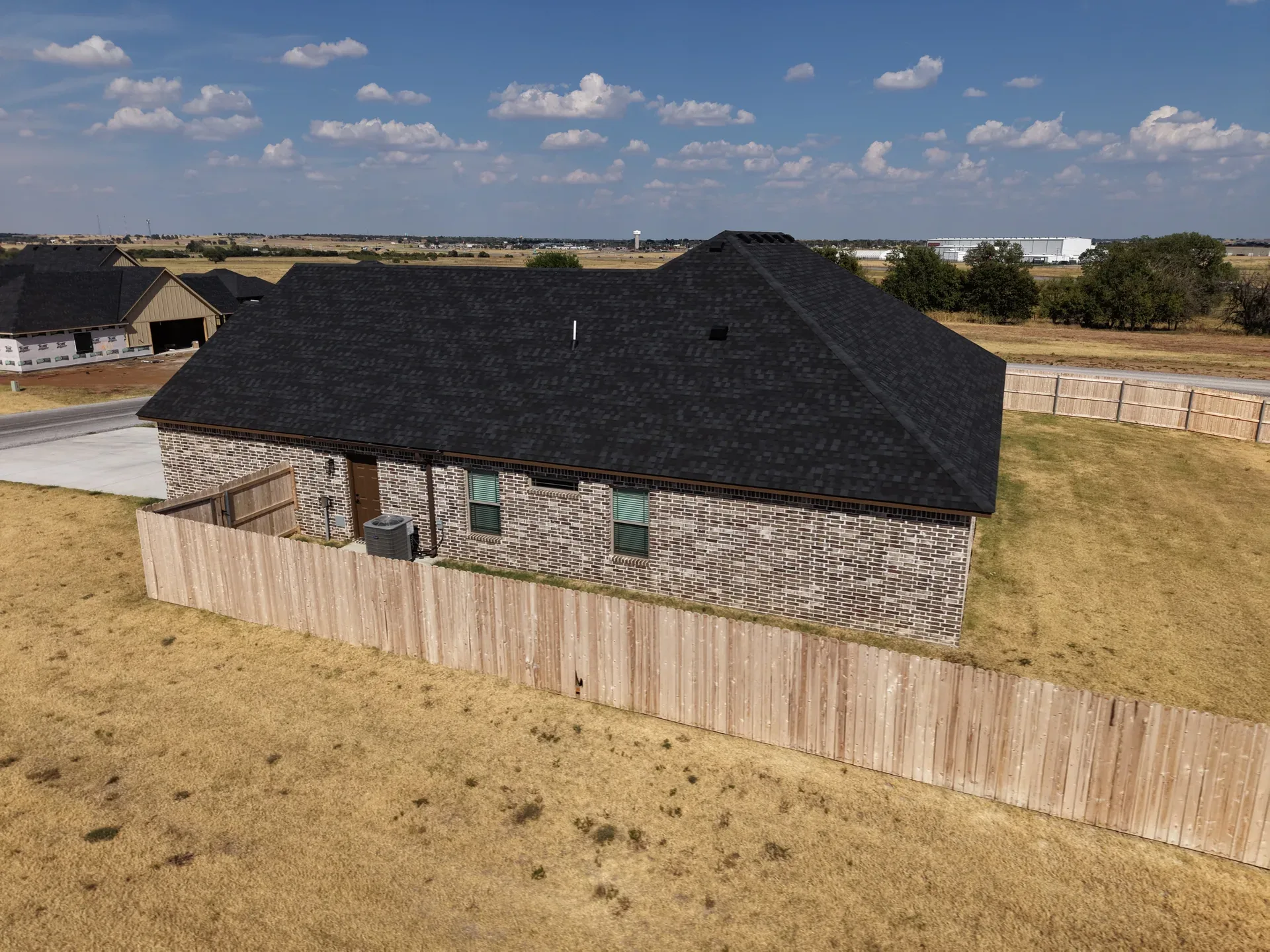 Aerial rear corner view of the ranch with privacy fence, HVAC unit, and driveway