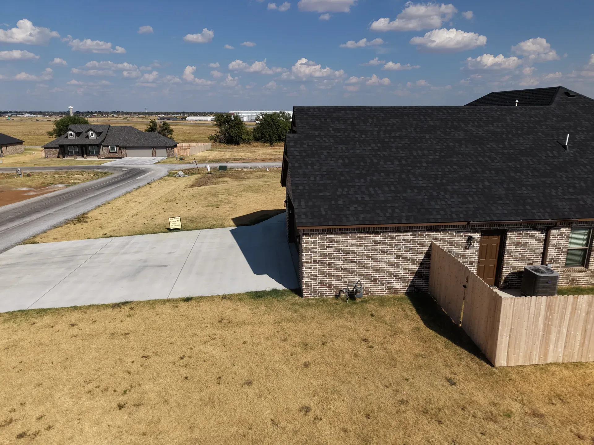 Aerial side profile of the single-story home showing roof, driveway, and fence