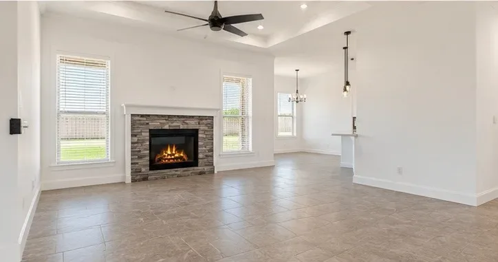 Living room with stone veneer fireplace surround, neutral tile flooring, and views into the dining area and kitchen