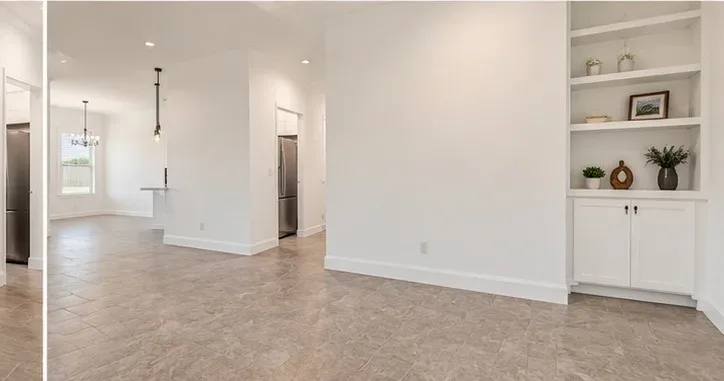 Open-concept living and dining area with white walls, light tile flooring, and built-in shelving