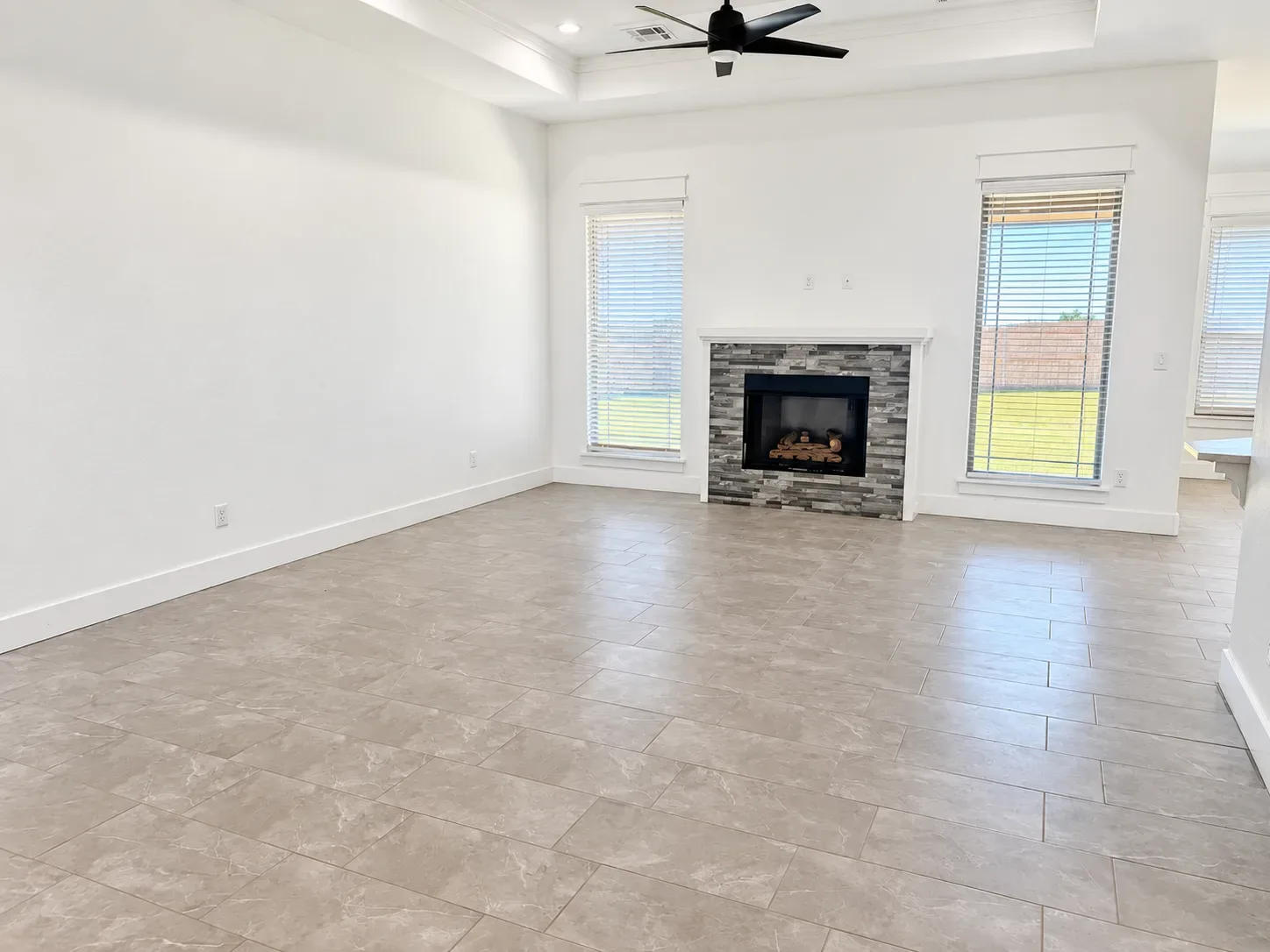 Living room with stone fireplace surround, white mantel, tray ceiling, and light tile flooring