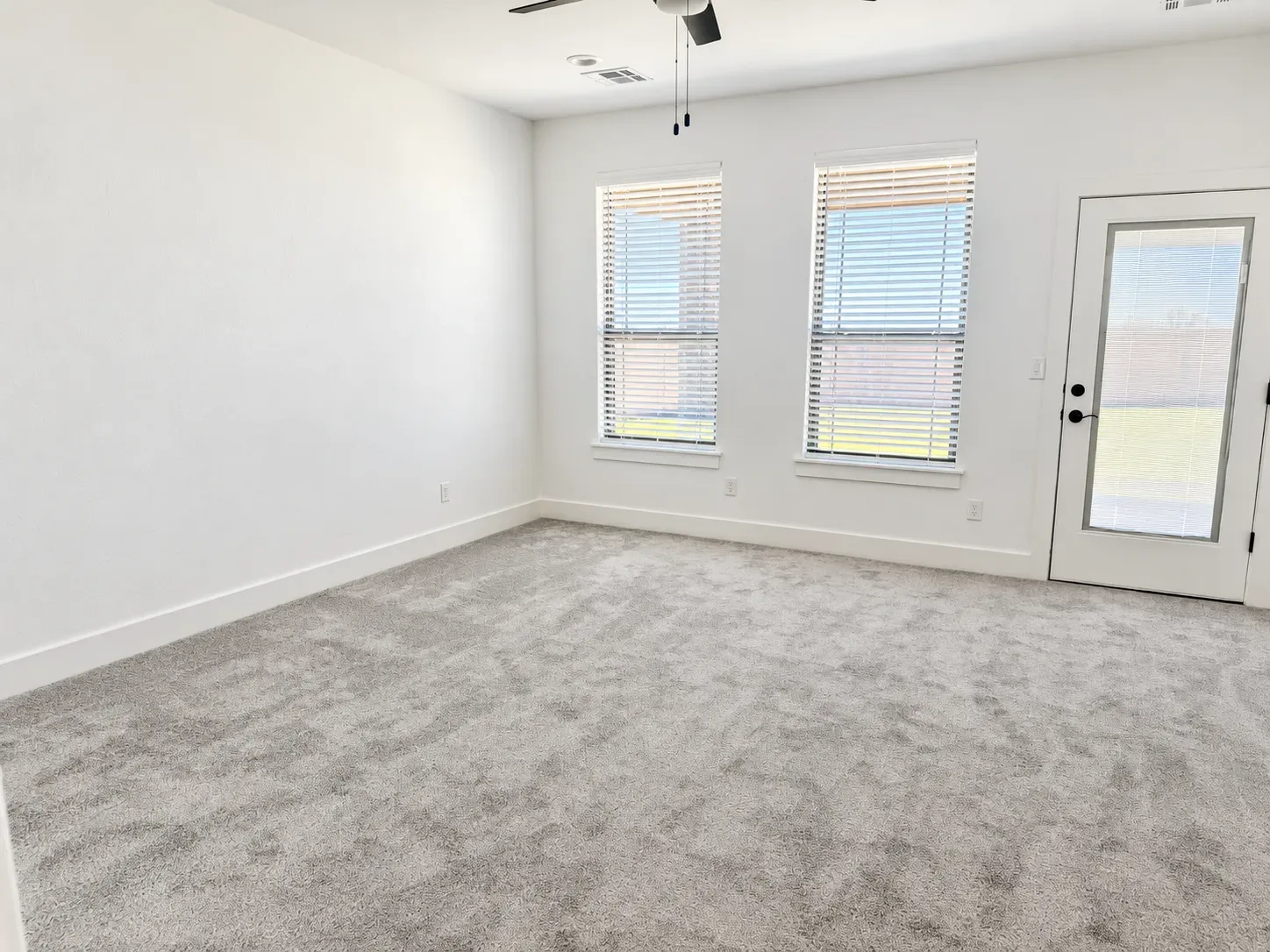 Bright interior space with white walls, gray carpet, large windows, and window blinds