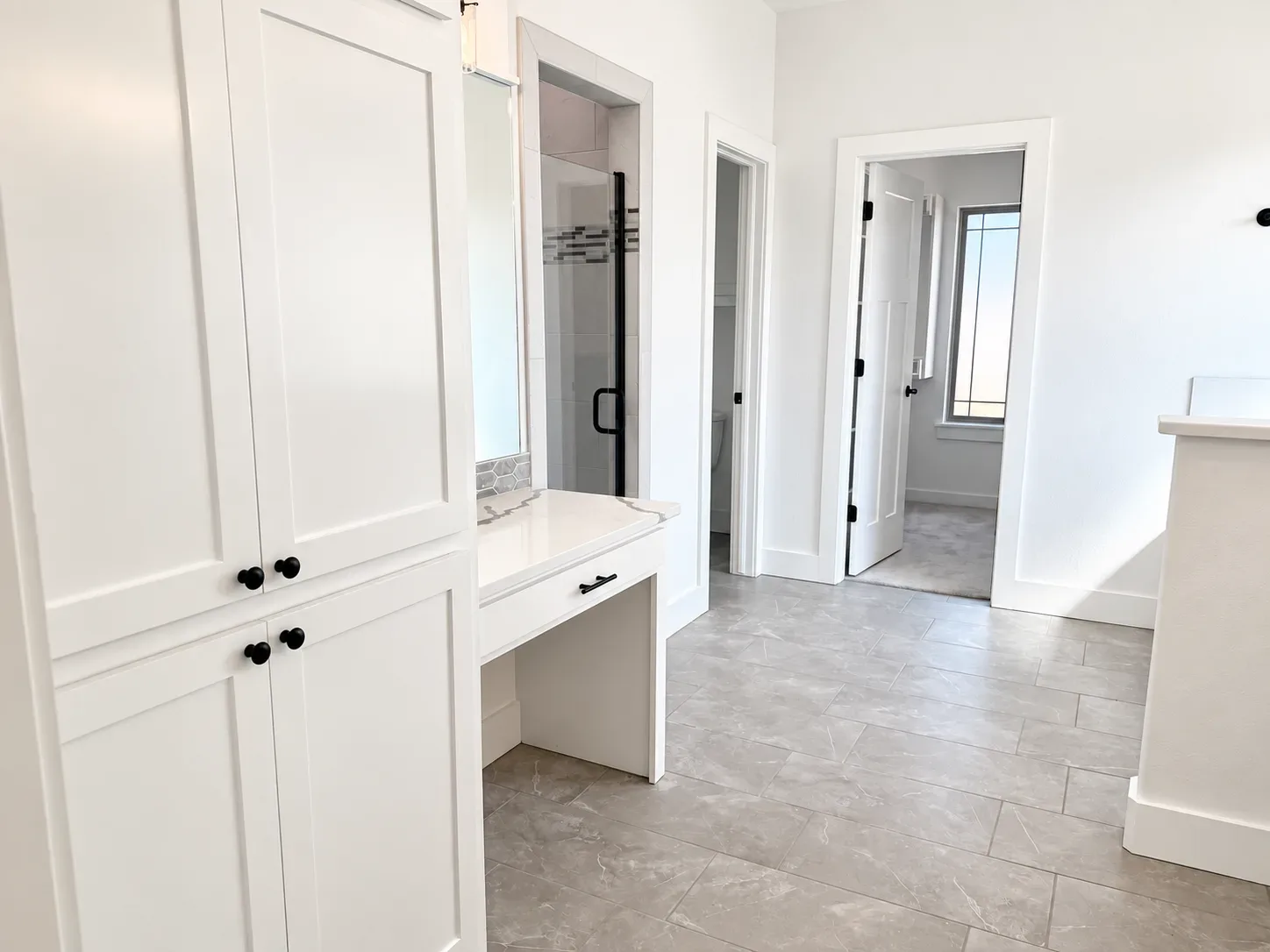 Bathroom vanity area with white shaker cabinetry, quartz vanity top, gray tile flooring, and a walk-in shower beyond
