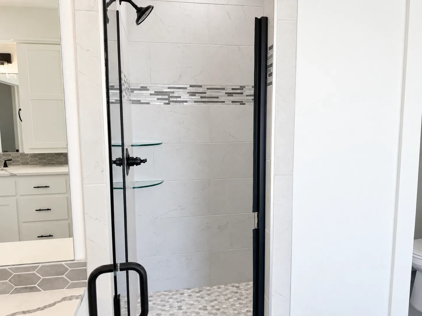 Walk-in shower with white subway tile, mosaic accent stripe, glass shelves, and matte black fixtures