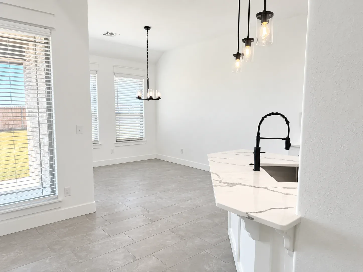Modern kitchen with white cabinetry, marble-look countertops, tile flooring, and a view into the adjoining dining room