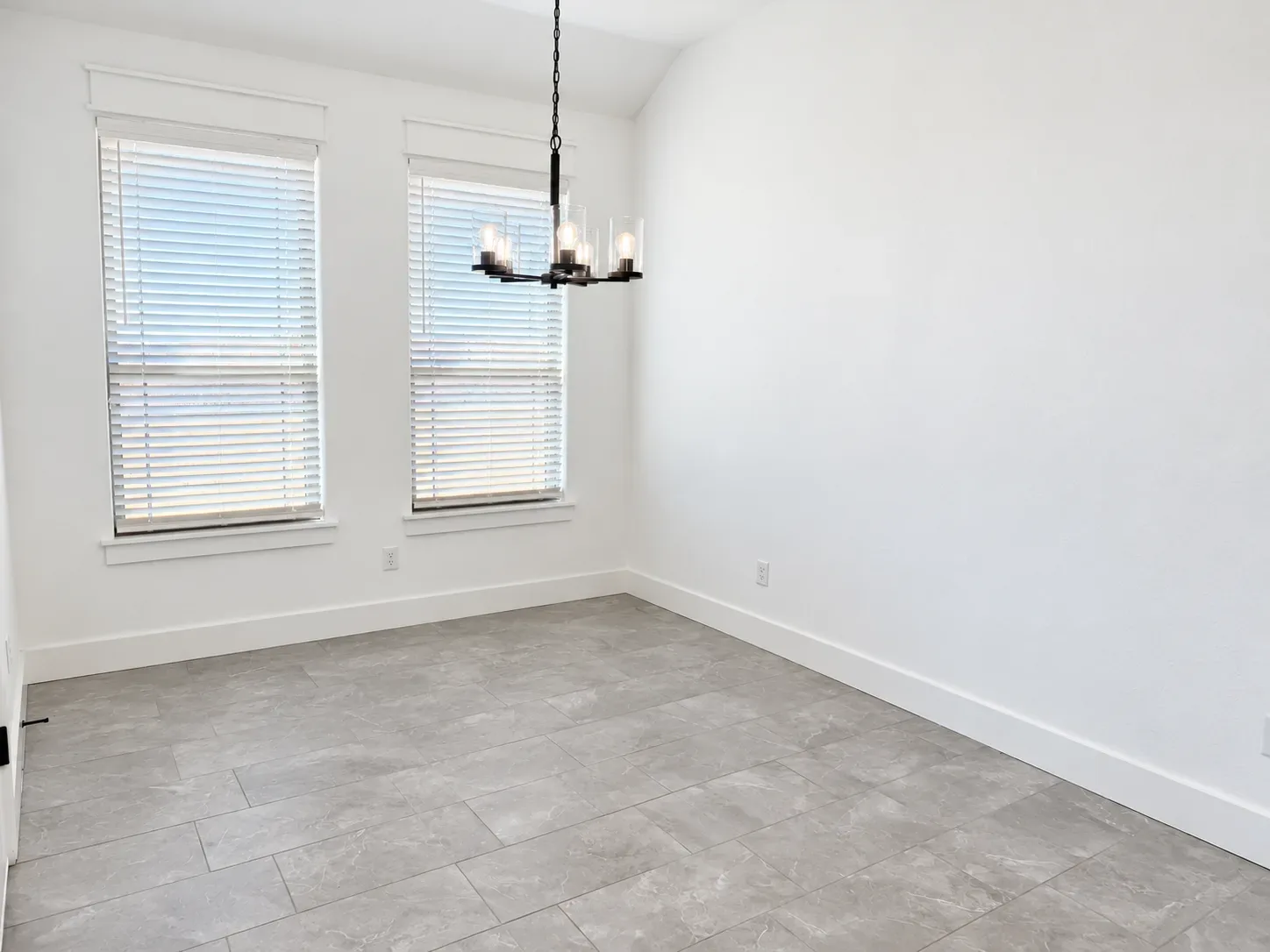 Dining room with white walls, light gray tile flooring, and a modern black metal chandelier