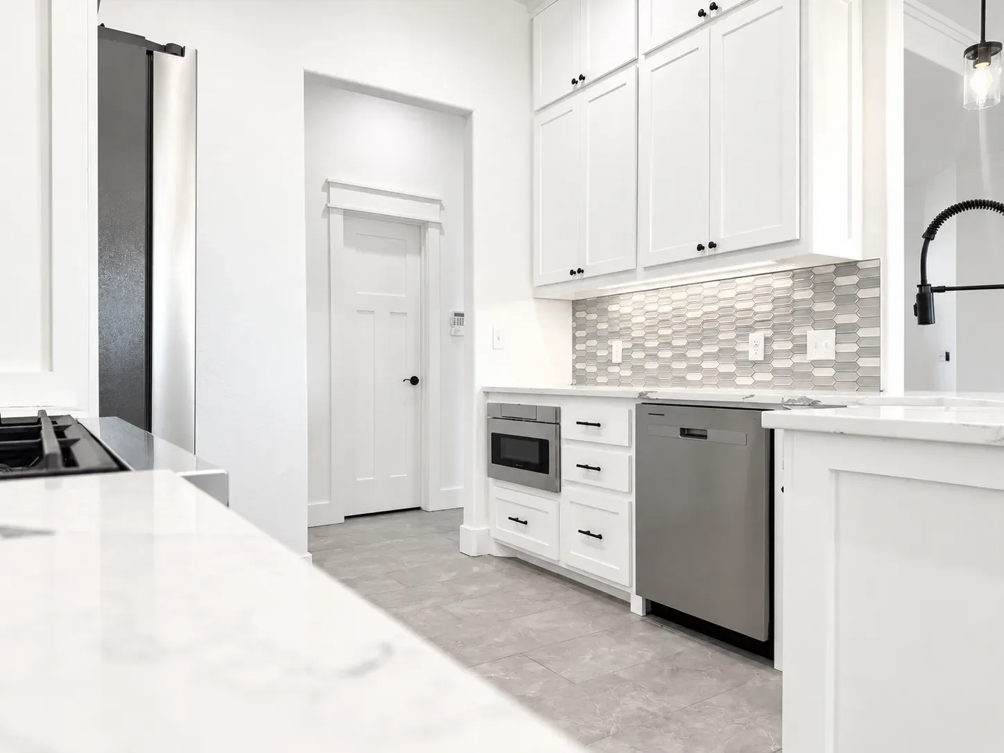 Modern white kitchen with shaker cabinetry, black hardware, quartz countertops, and patterned tile backsplash