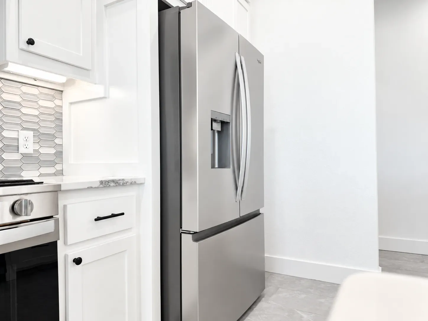 Kitchen close-up with stainless steel French door refrigerator, white shaker cabinetry, and gray backsplash tile