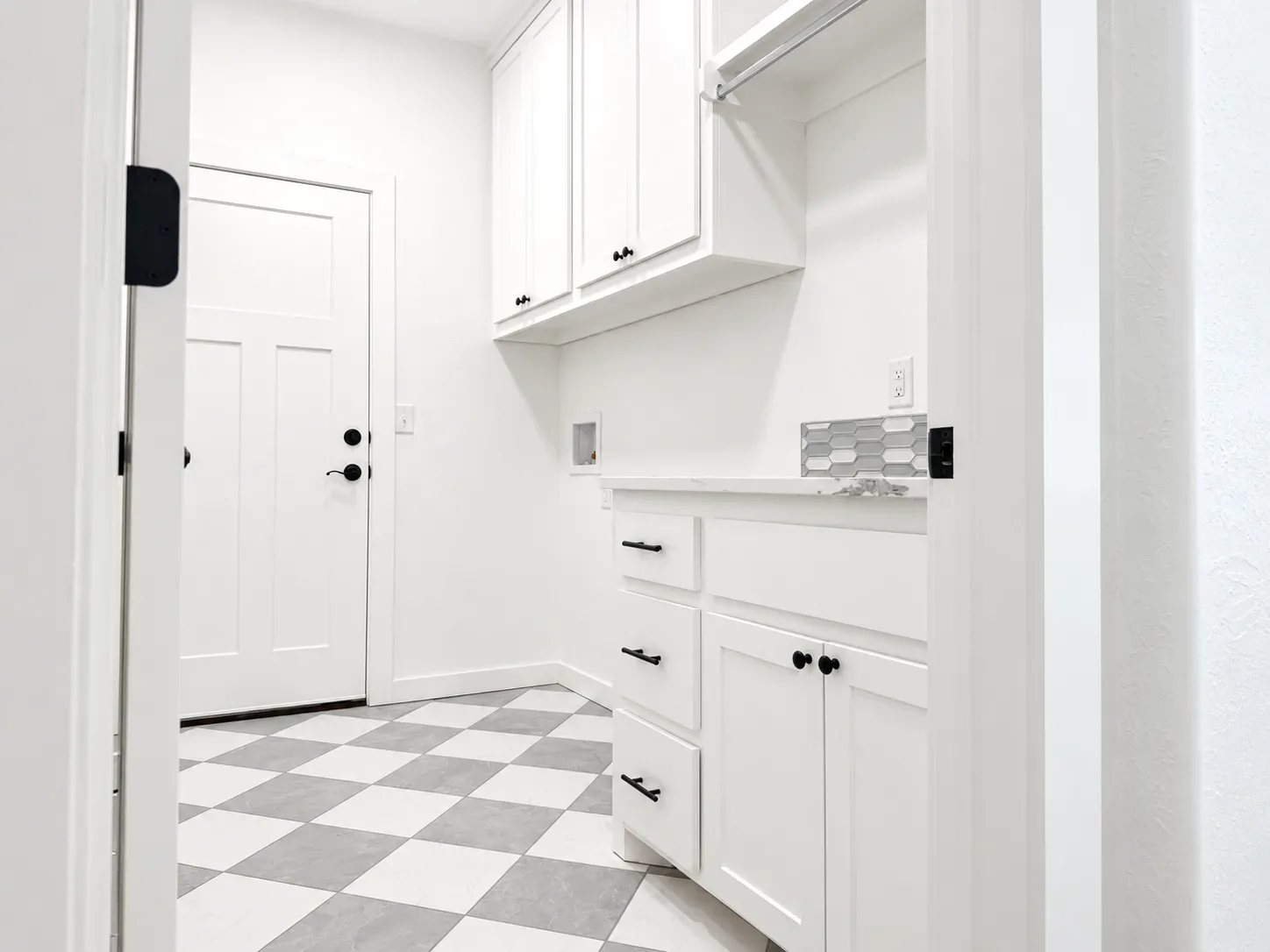 Laundry room with white shaker cabinets, matte black hardware, and checkered tile flooring