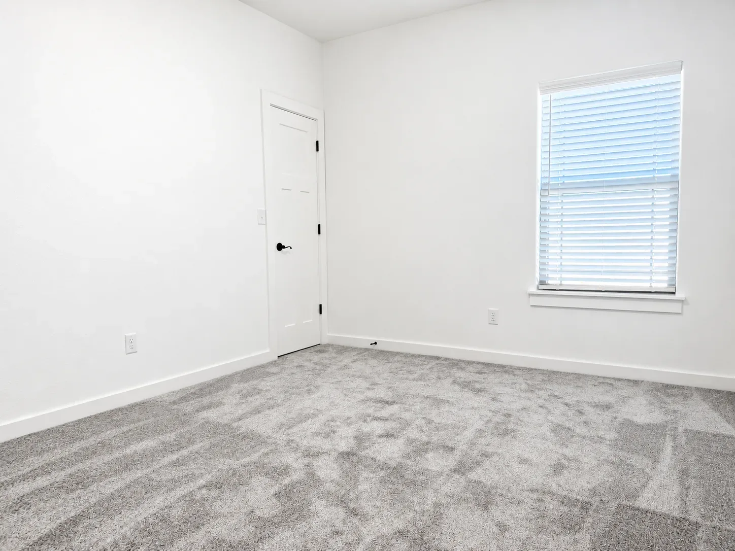 Bedroom with white walls, gray carpet, and a modern white door