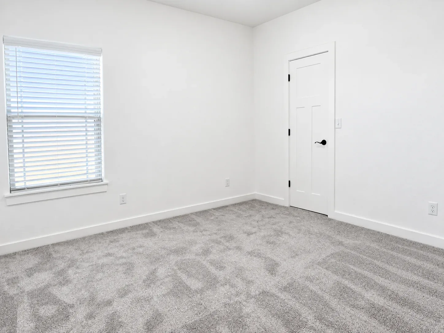 Bright bedroom with white walls, gray wall-to-wall carpeting, and white window blinds