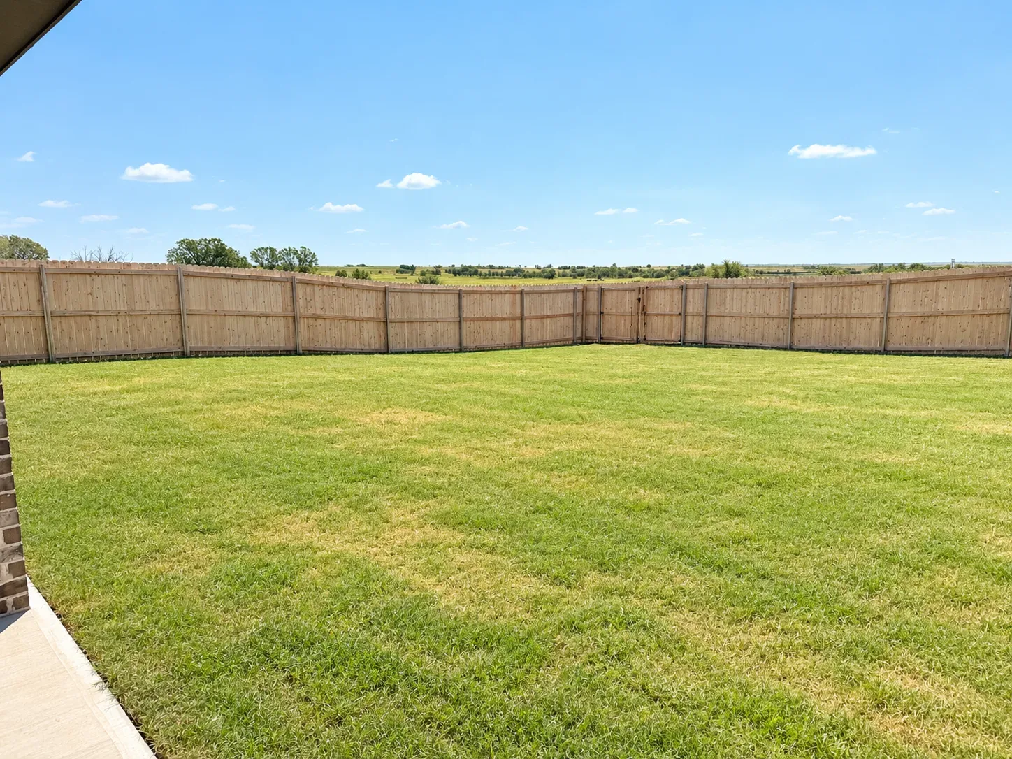 Spacious fenced backyard with a large grassy lawn enclosed by a light-wood privacy fence
