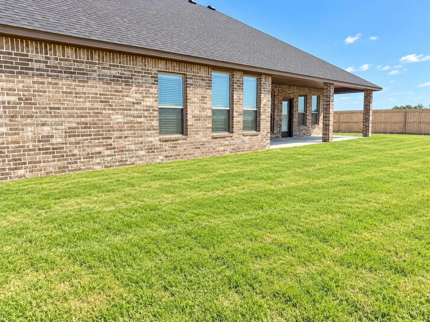 Backyard view toward the rear of the brick home with covered patio and manicured lawn