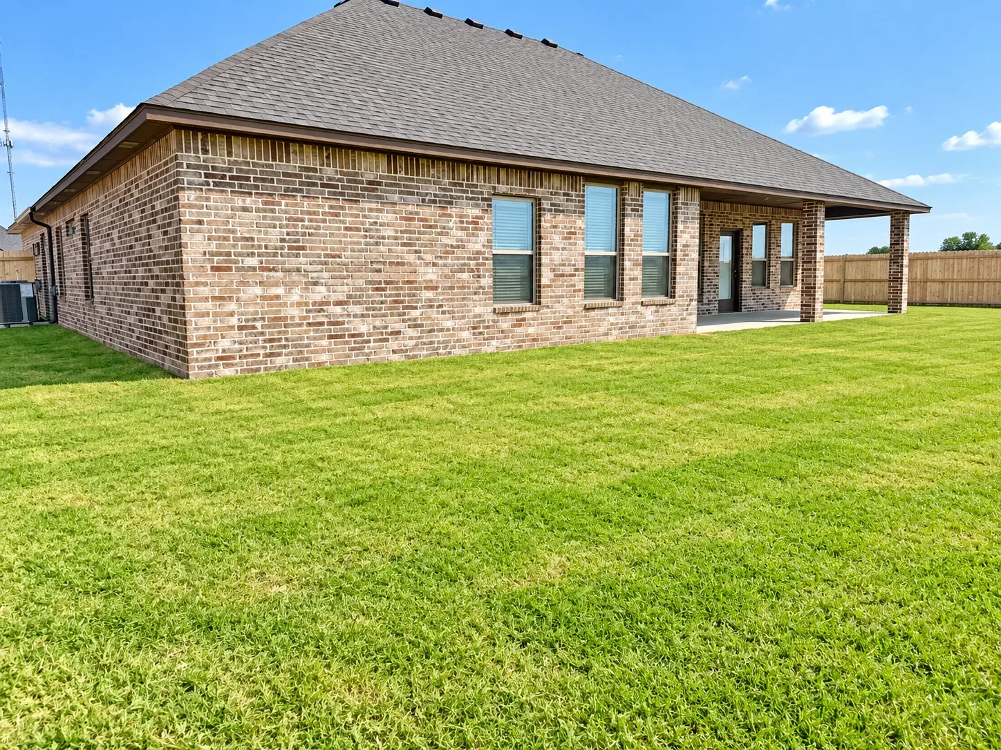 Rear exterior of the single-story brick home with covered patio under a clear sky