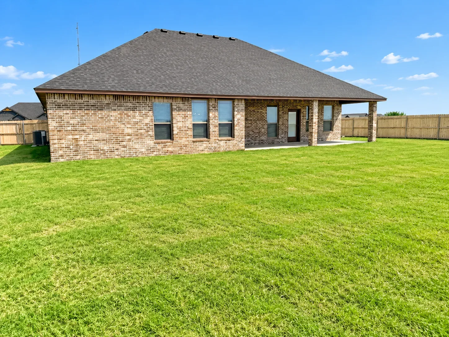 Backyard view of the tan brick ranch with expansive lawn, privacy fence, and HVAC unit