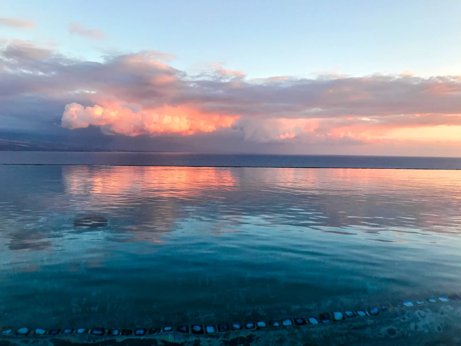 An infinity pool reflecting a warm sunset sky over the ocean