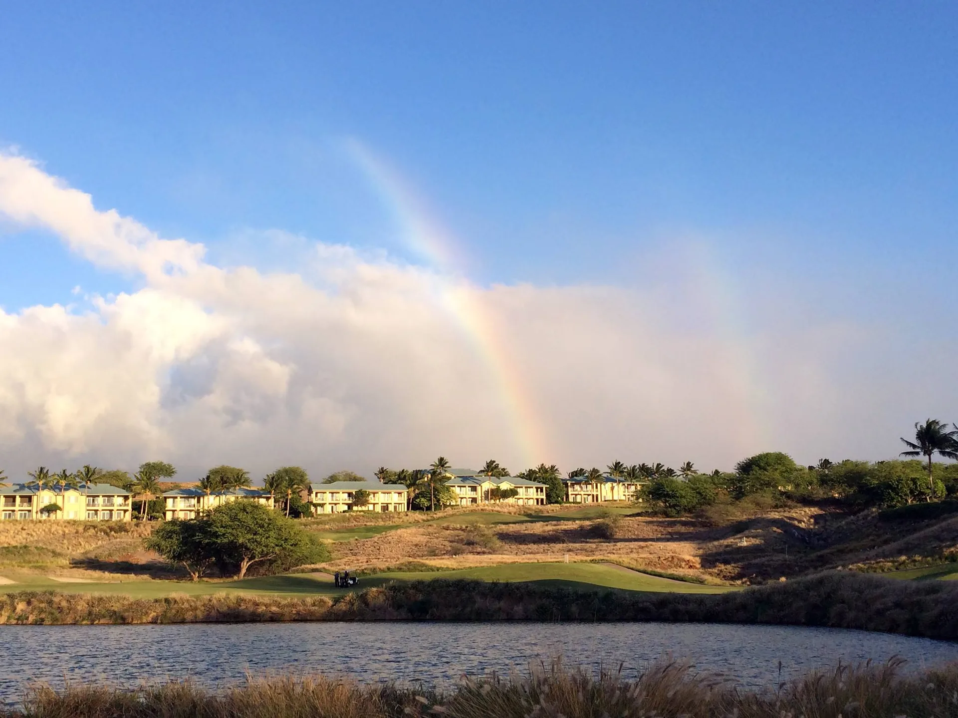 Golf course terrain with a pond and a rainbow in the sky