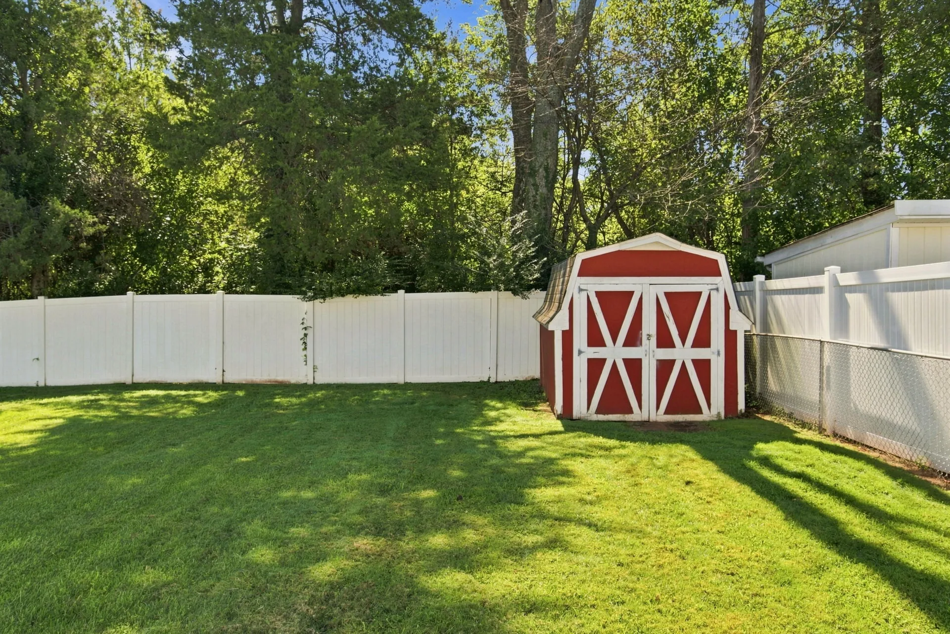 Backyard with red and white gambrel-style storage shed and tree line