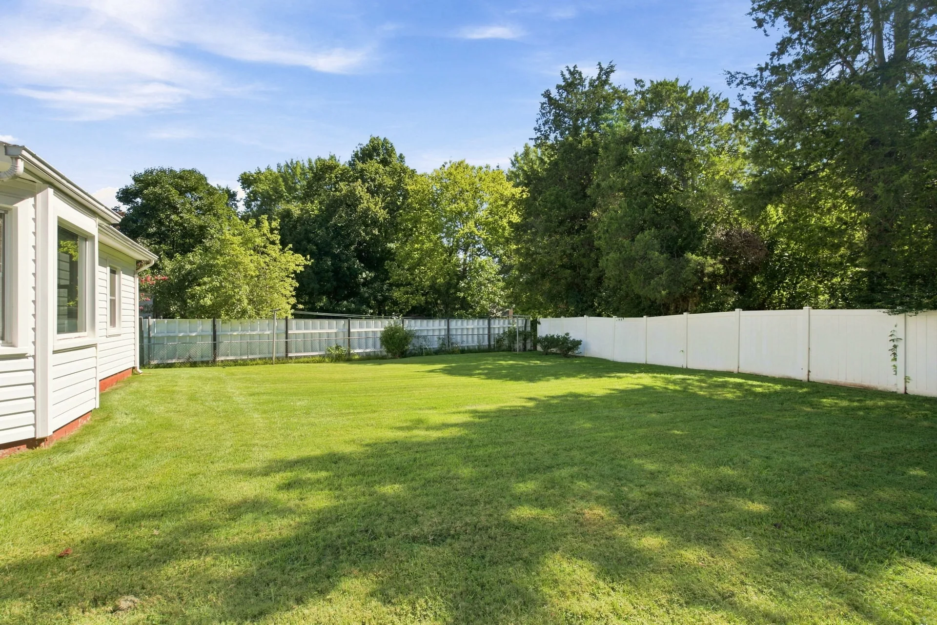 Backyard with a large flat lawn and white vinyl privacy fence