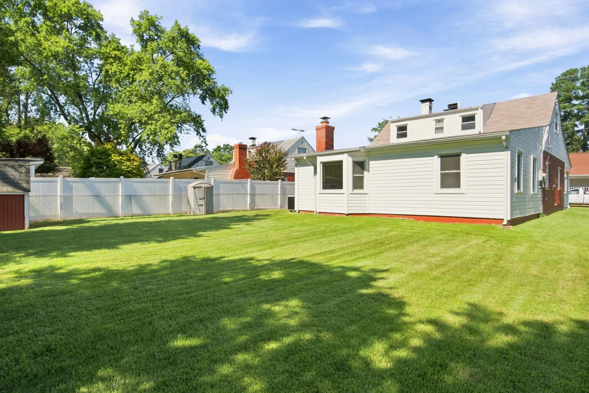 Backyard with white privacy fence, brick chimney, and sunny sky