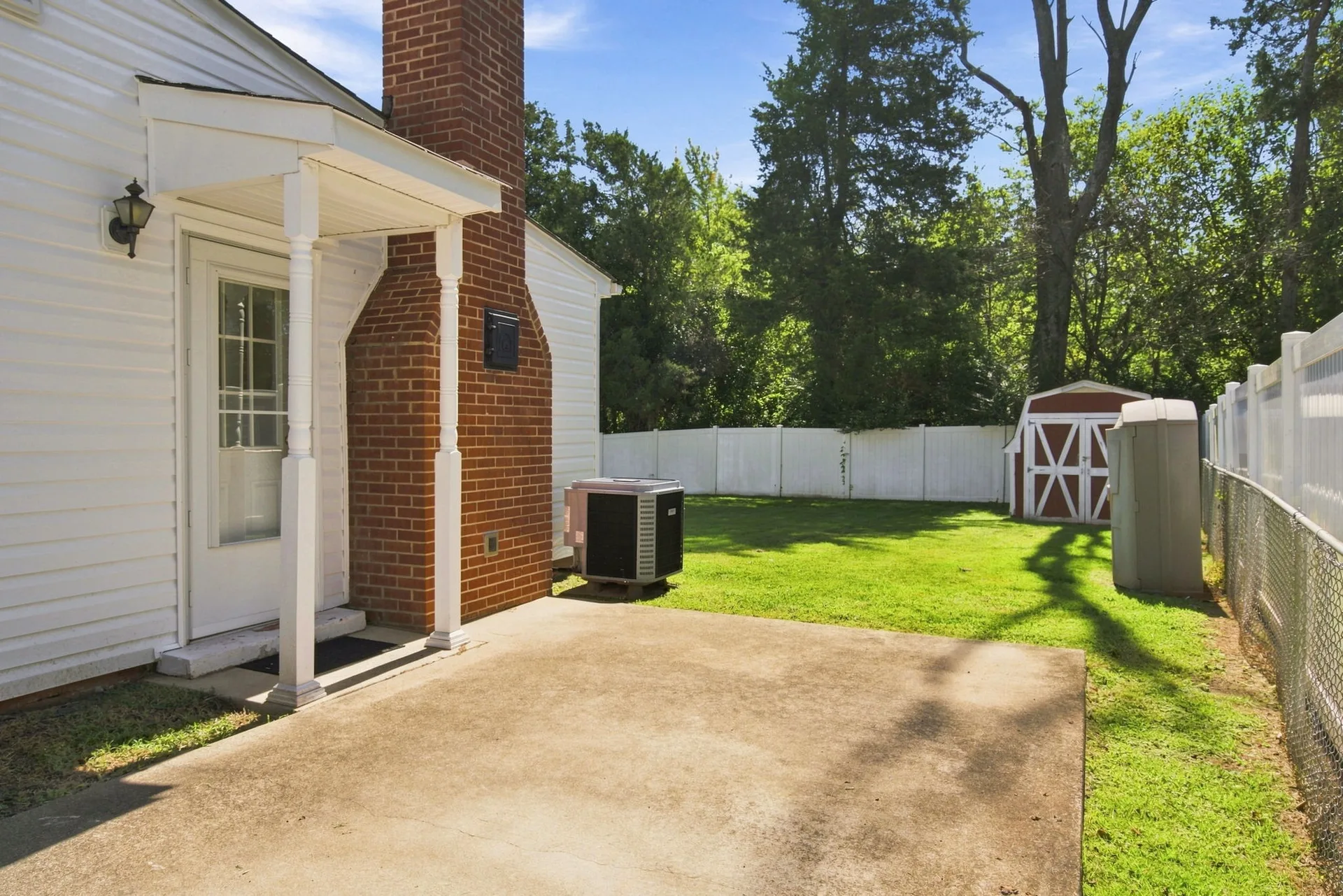Concrete patio behind the house with mature trees and white fence