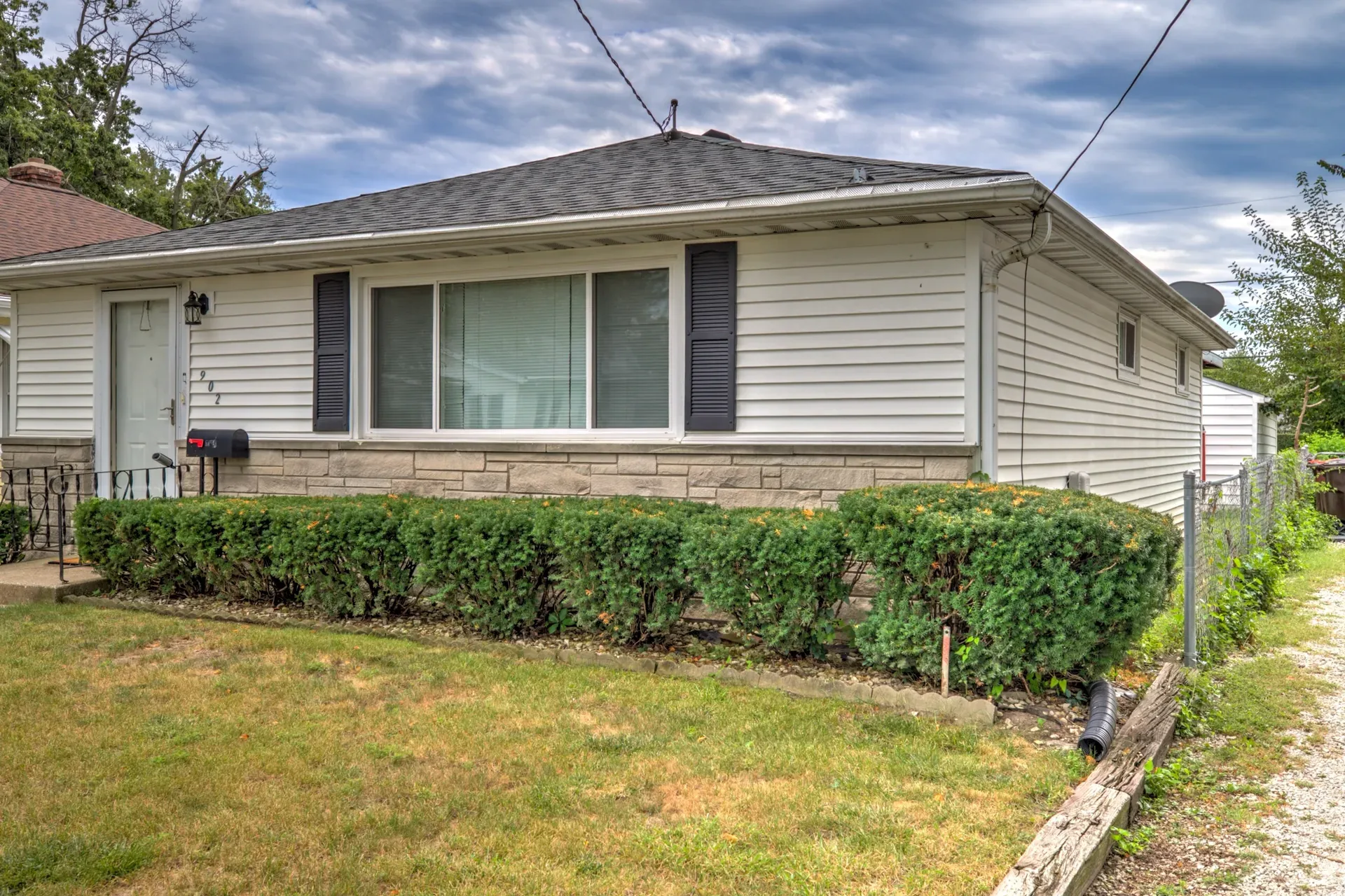 Front view of the ranch home with hedge line, mailbox, and gravel driveway