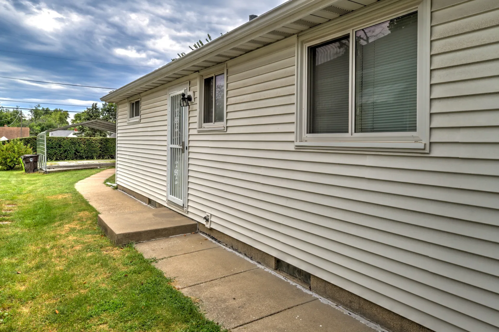Side exterior with concrete walkway and green lawn along the house