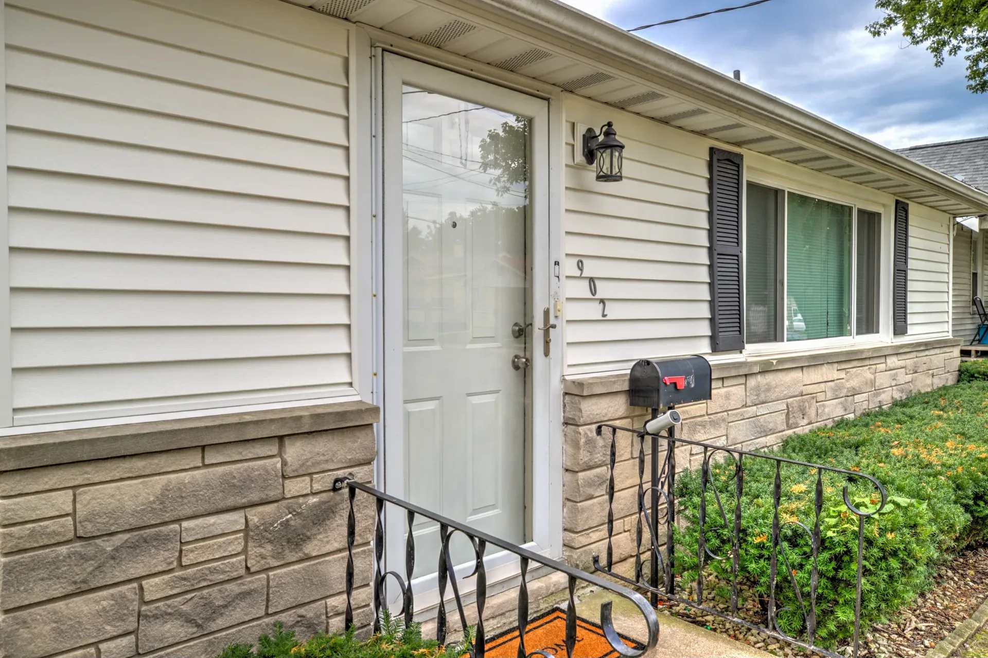 Front entry with stone veneer base, black railing, and a glass storm door