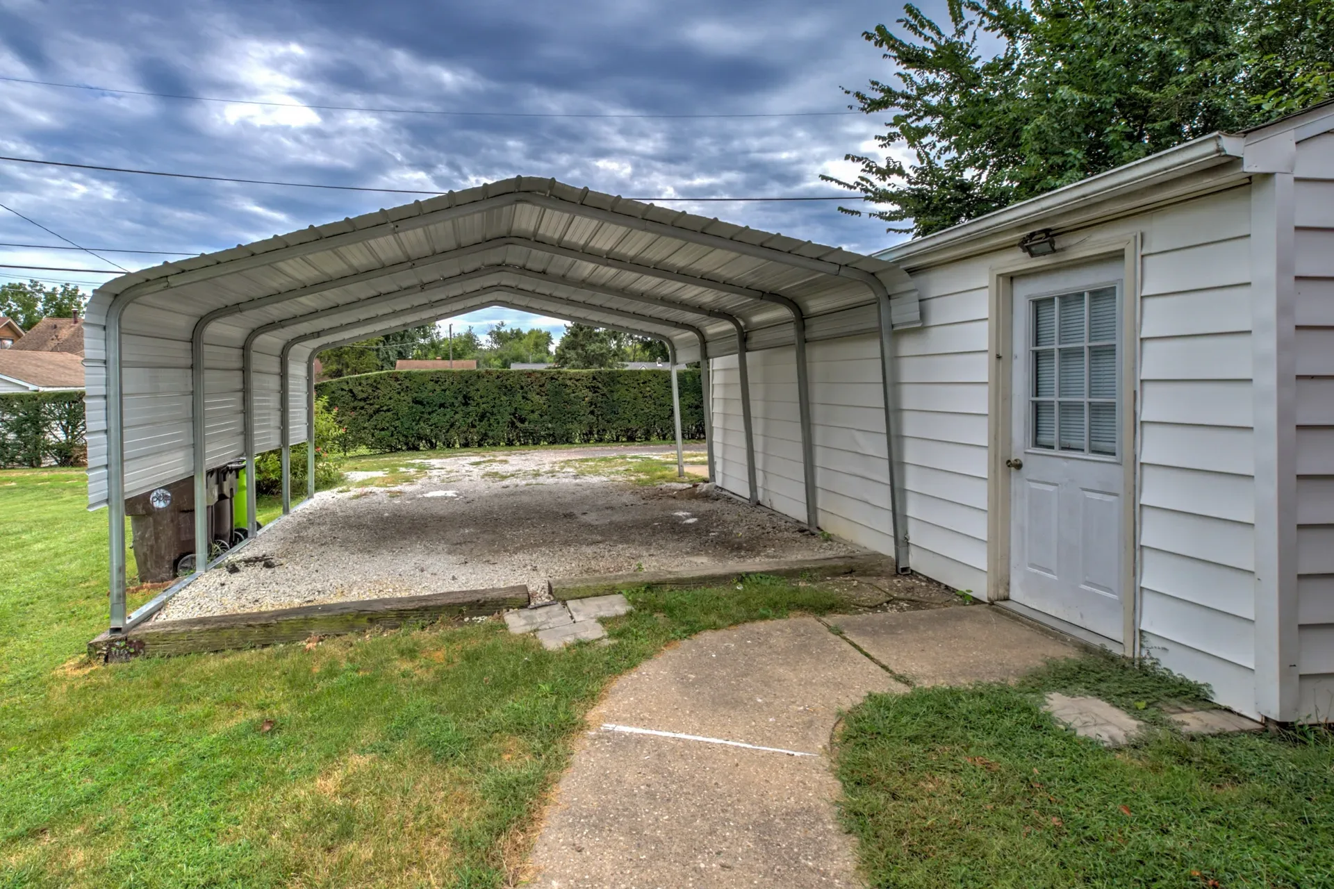 Backyard carport with gravel parking area behind the home