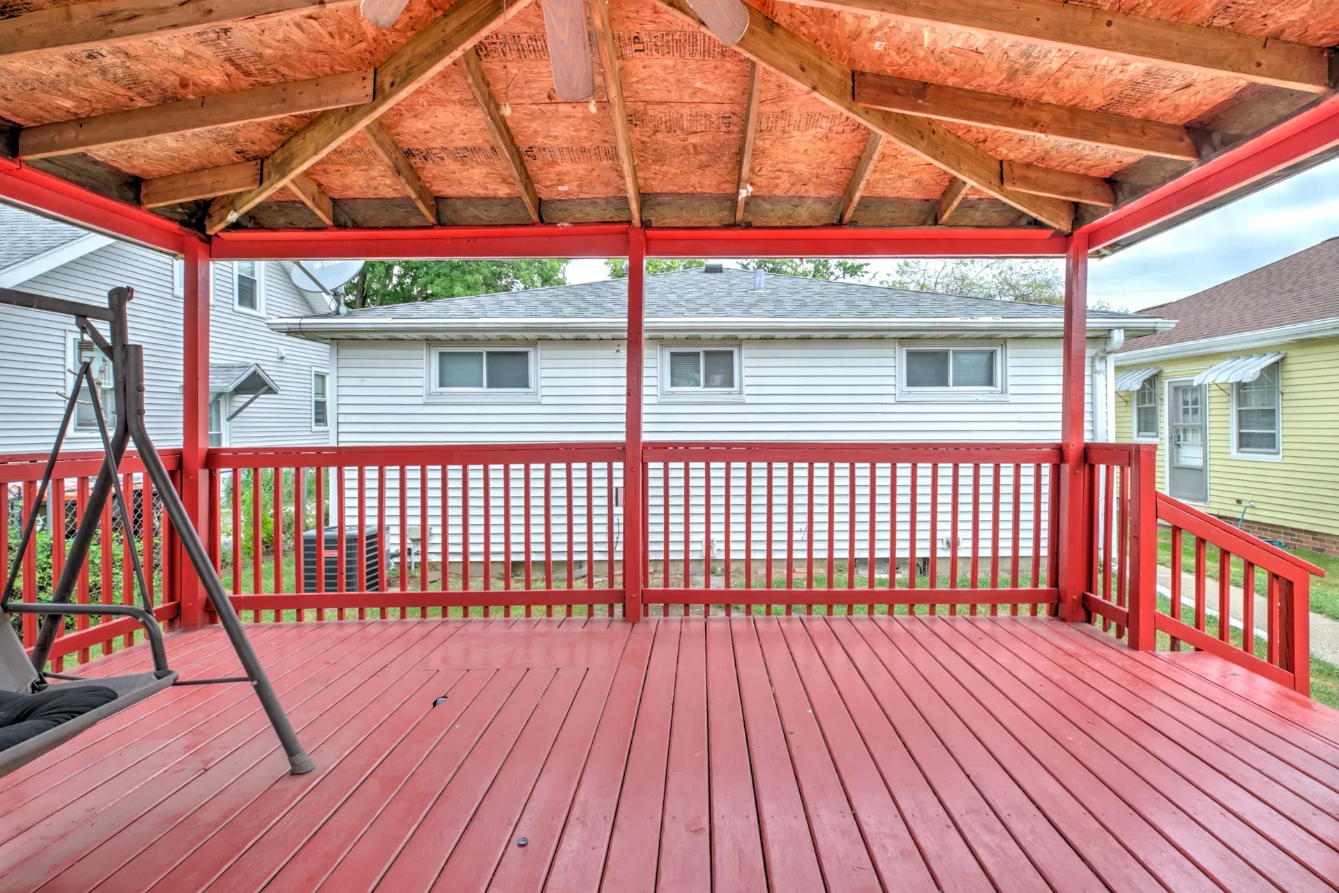 Covered wooden deck with exposed rafters overlooking the backyard lawn