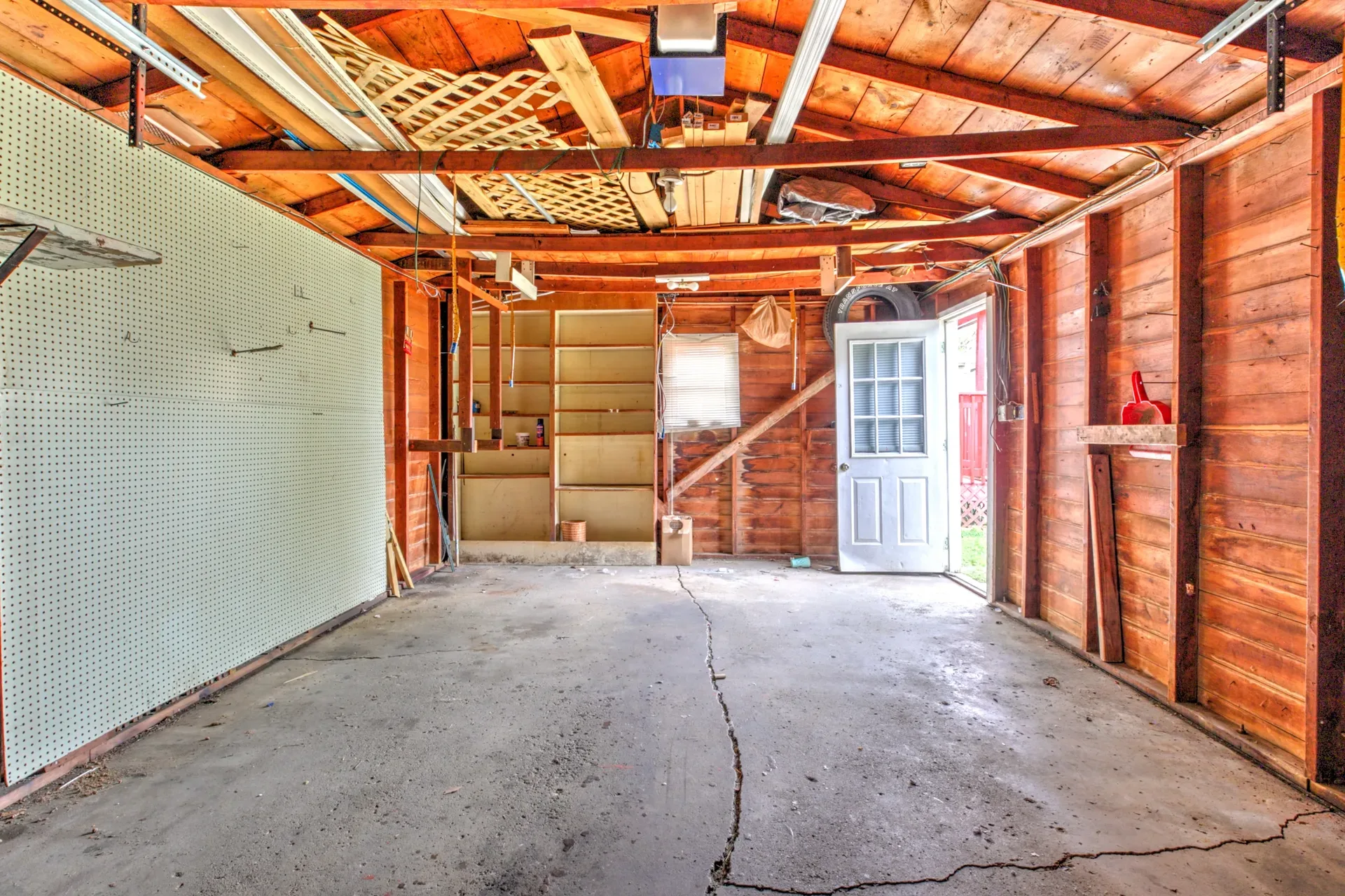 Garage interior with exposed wood framing, shelving, and a side door with daylight