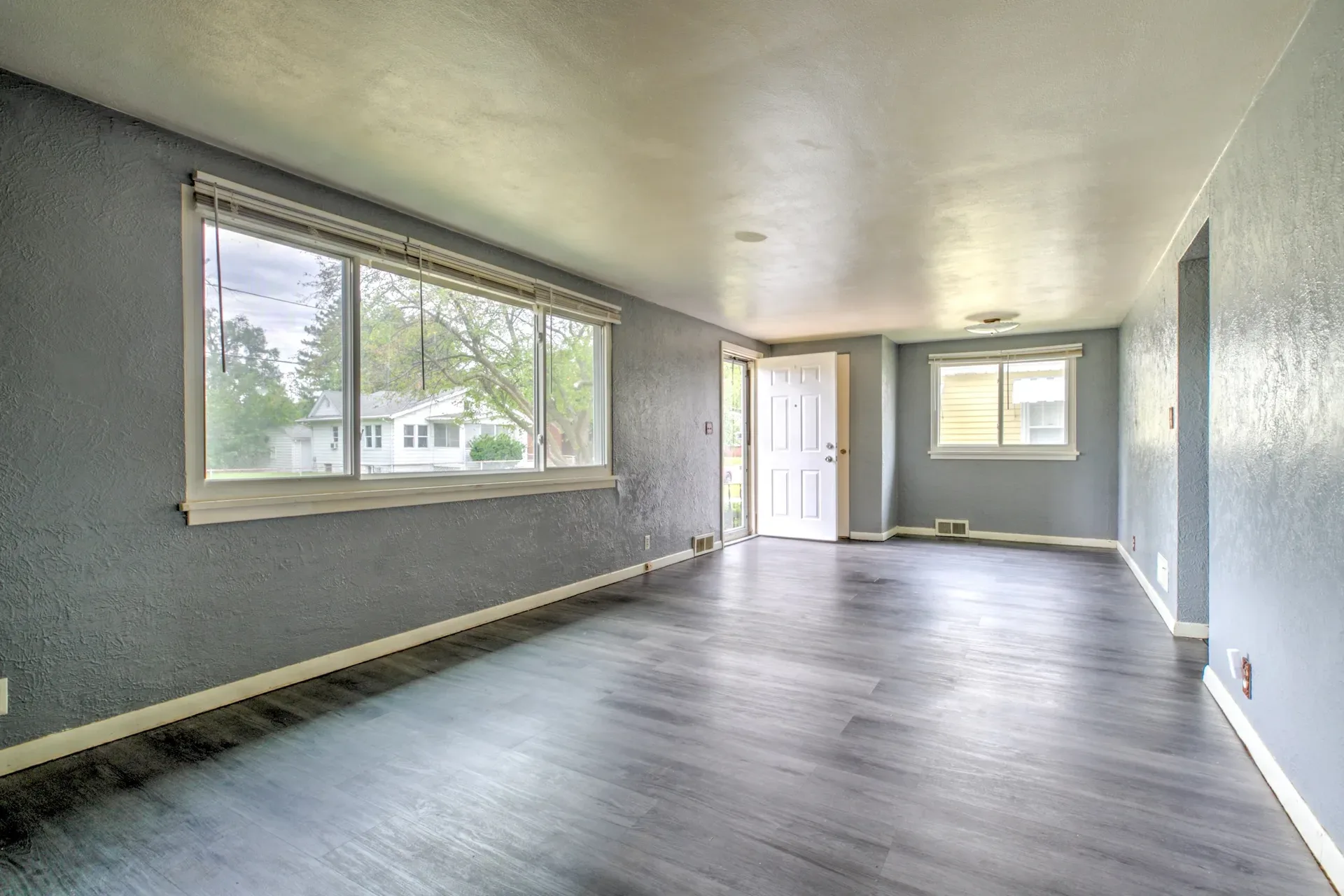 Bright, vacant living room with grey walls, white trim, and wood-look plank flooring