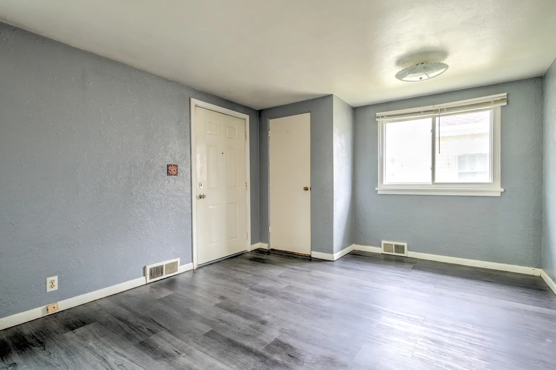 Living room with grey walls, wood-look flooring, and a window letting in natural light