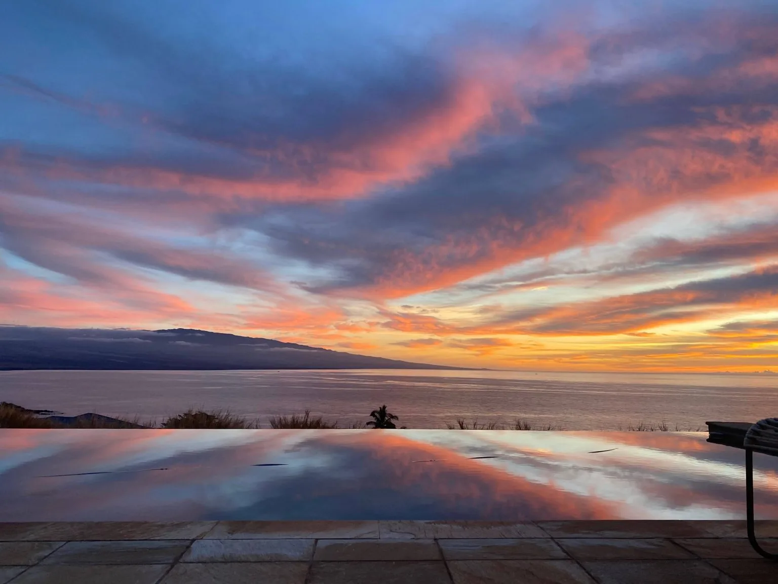 An infinity pool reflecting vibrant pink and orange post-sunset skies