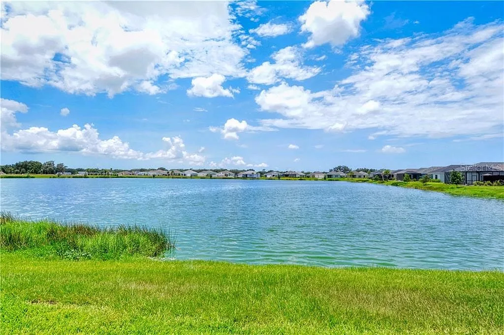 Backyard lawn leading to a calm pond with homes across the water