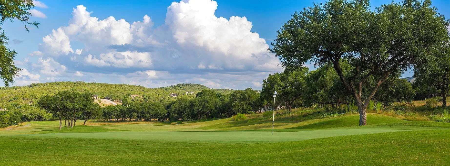 Scenic view of the River Crossing golf course with rolling green fairways, mature oak trees and a clear blue sky