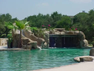 River Crossing Club resort pool with a large rock work grotto and waterslide surrounded by mature trees