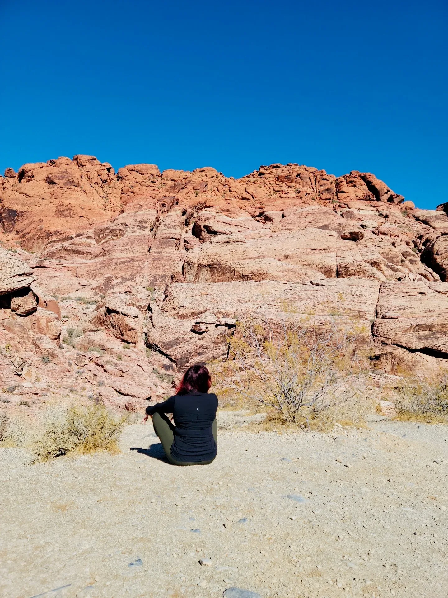 Samantha Medeiros seated on a trail facing the red rock cliff face at Red Rock Canyon